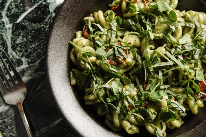 Close up of green herb coated trottole pasta in a dark bowl. Courtesy of Poeta