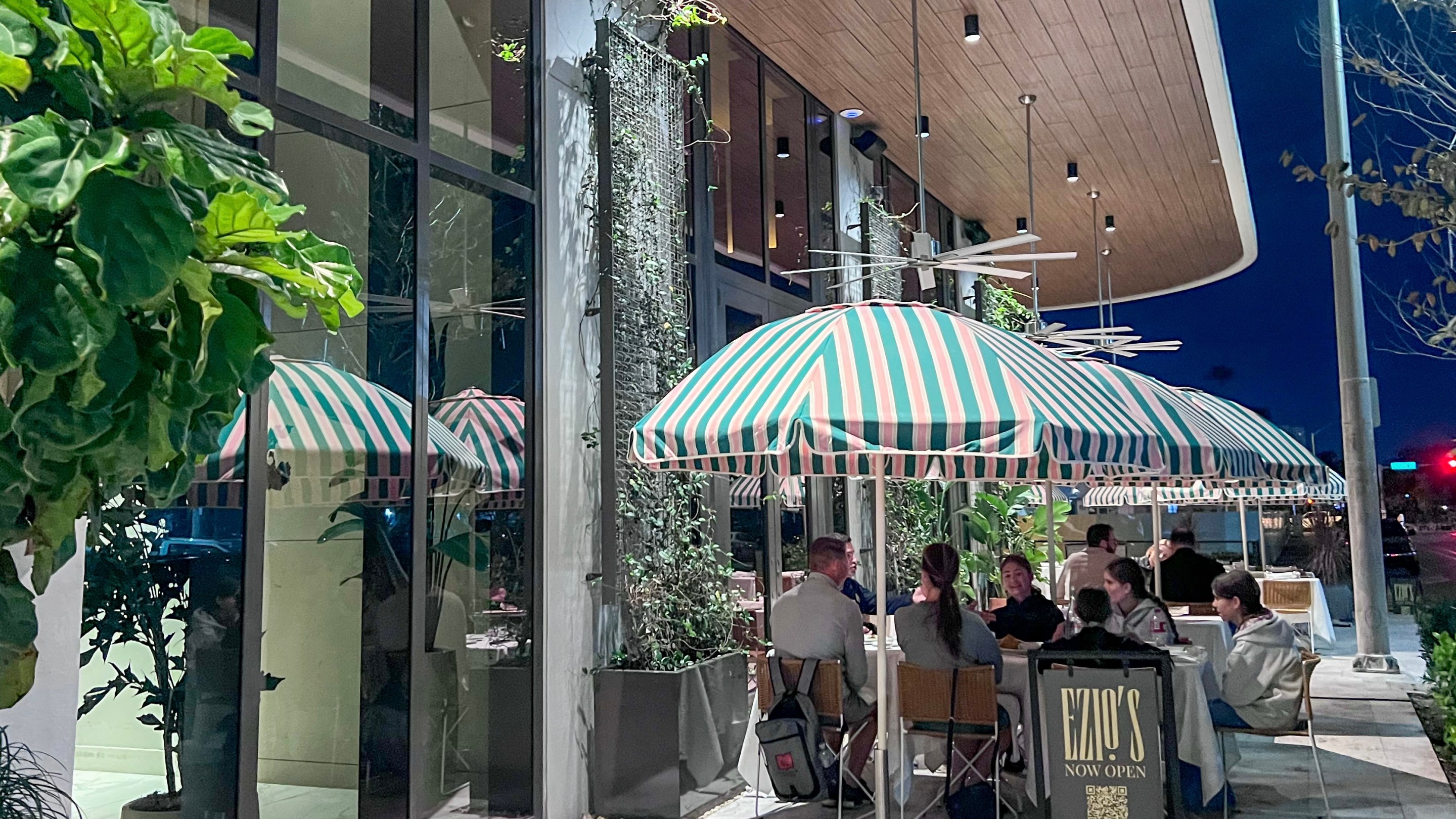 Exterior of Ezio’s in Miami Beach with striped umbrellas and outdoor dining at night