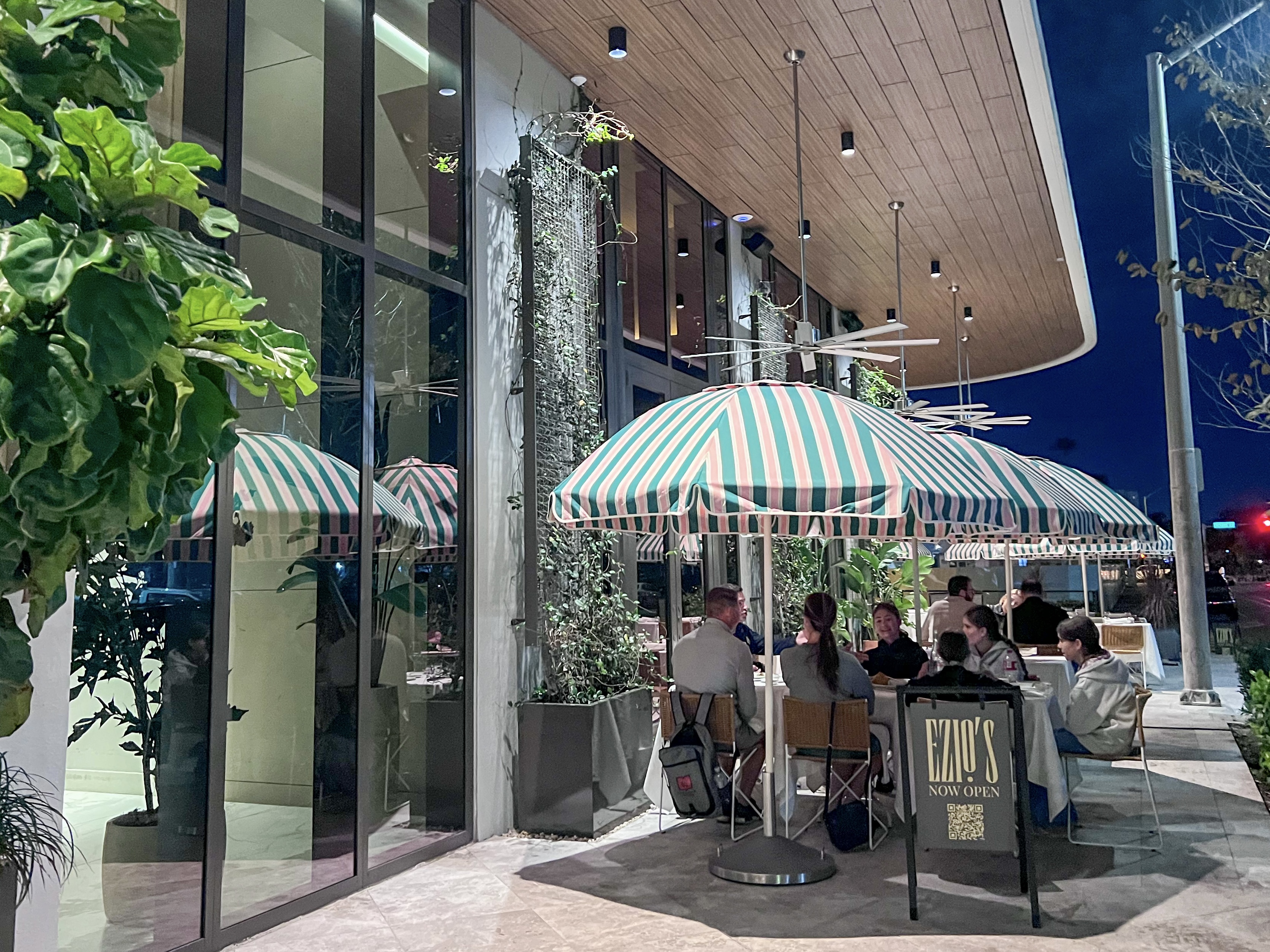Exterior of Ezio’s in Miami Beach with striped umbrellas and outdoor dining at night