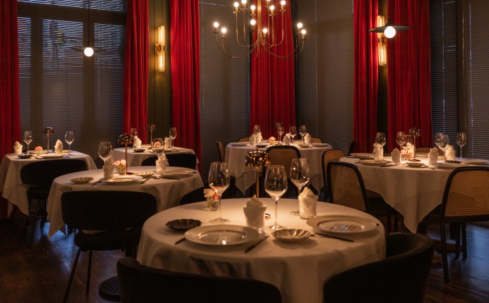 Elegant dining room at TUCCI New York with red velvet drapes, round tables and chandelier lighting.