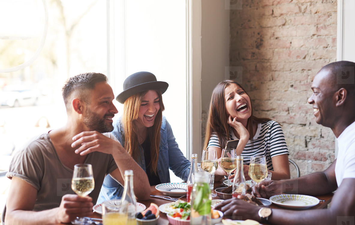 Friends around a table eating and drinking wine while laughing.