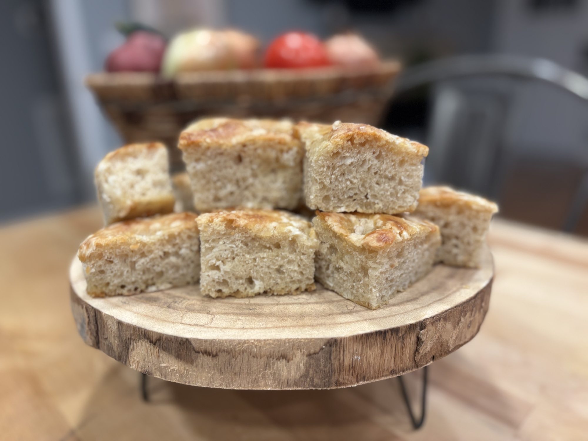 Square slices of sourdough discard focaccia stacked on a wooden serving stand.