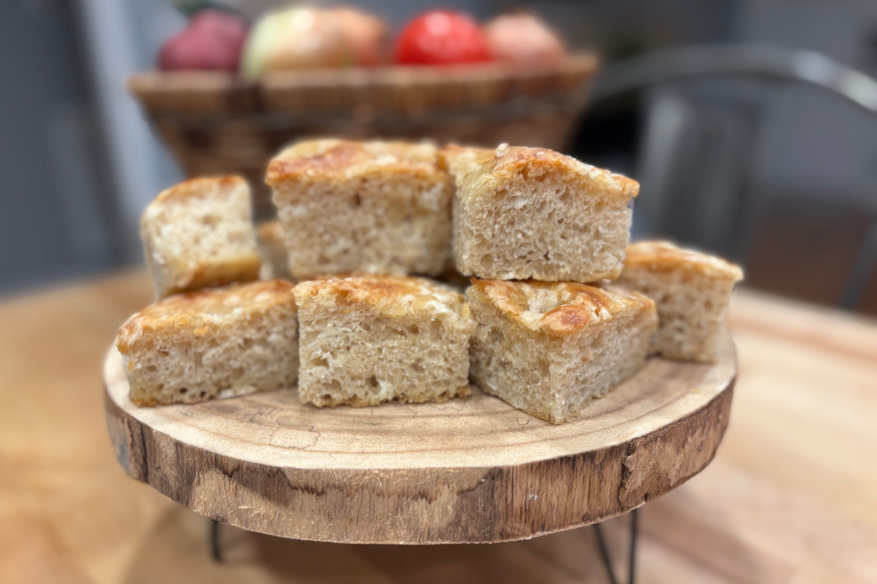 Square slices of sourdough discard focaccia stacked on a wooden serving stand.