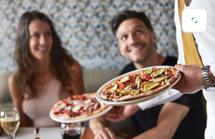 Server presenting pizza to guests dining at Alfredo’s Pizzeria on Princess Cruises