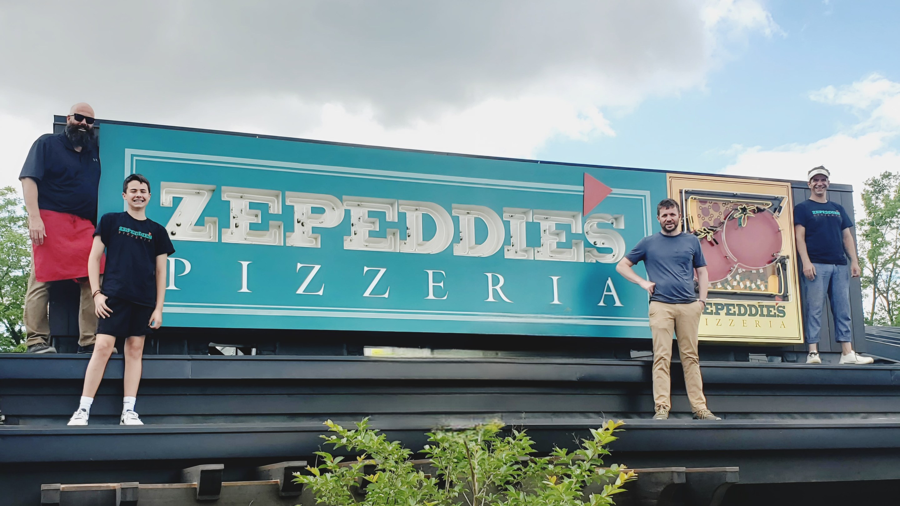 Team members standing on the rooftop beside the Zepeddie’s Pizzeria sign in Charlotte