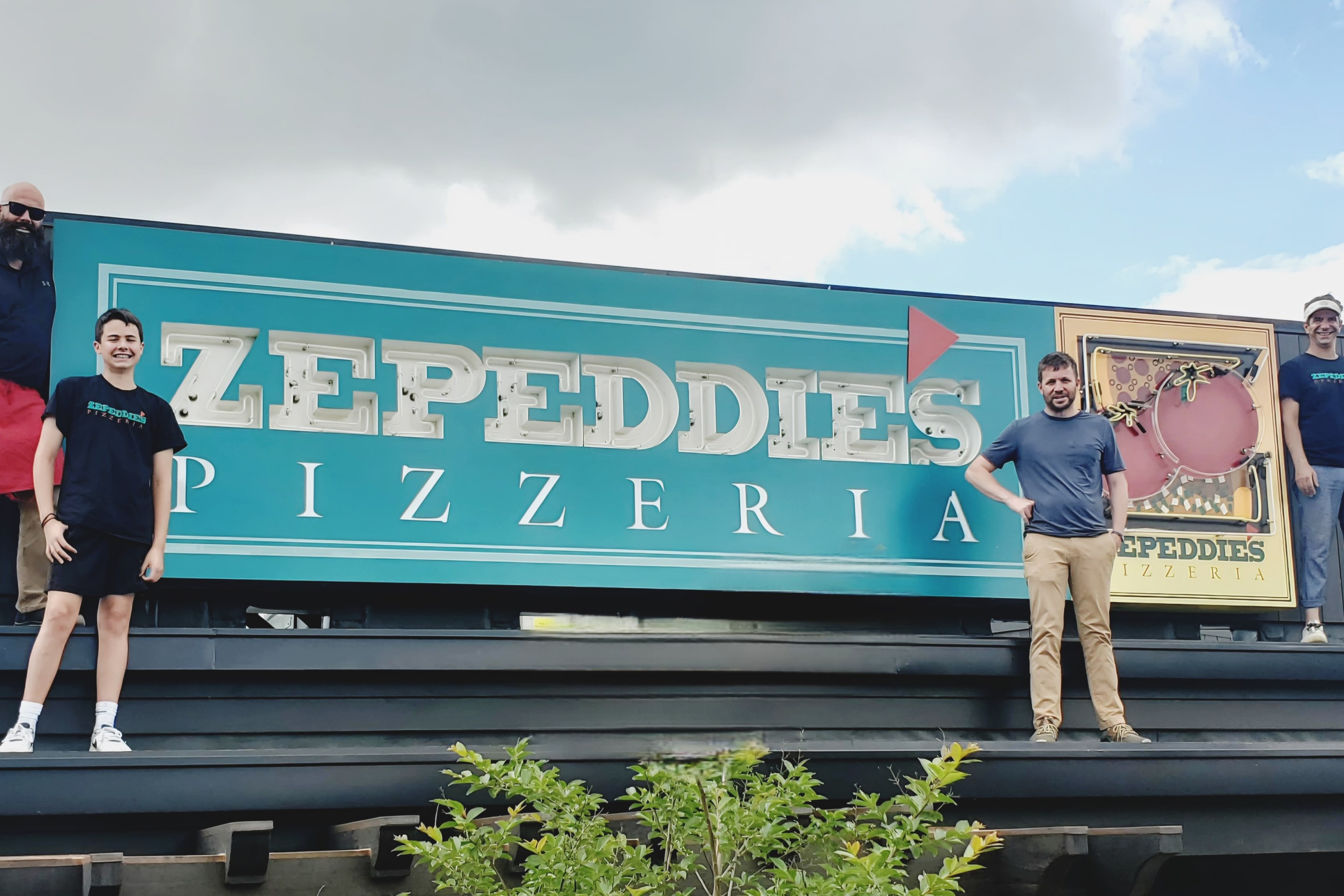 Team members standing on the rooftop beside the Zepeddie’s Pizzeria sign in Charlotte