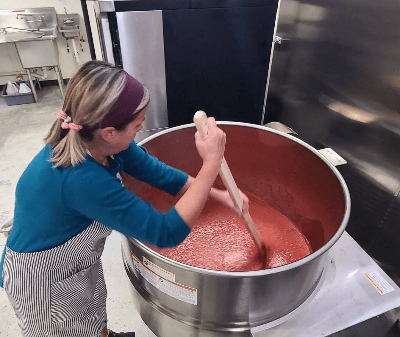 Stirring a large pot of tomato sauce in a commercial kitchen.