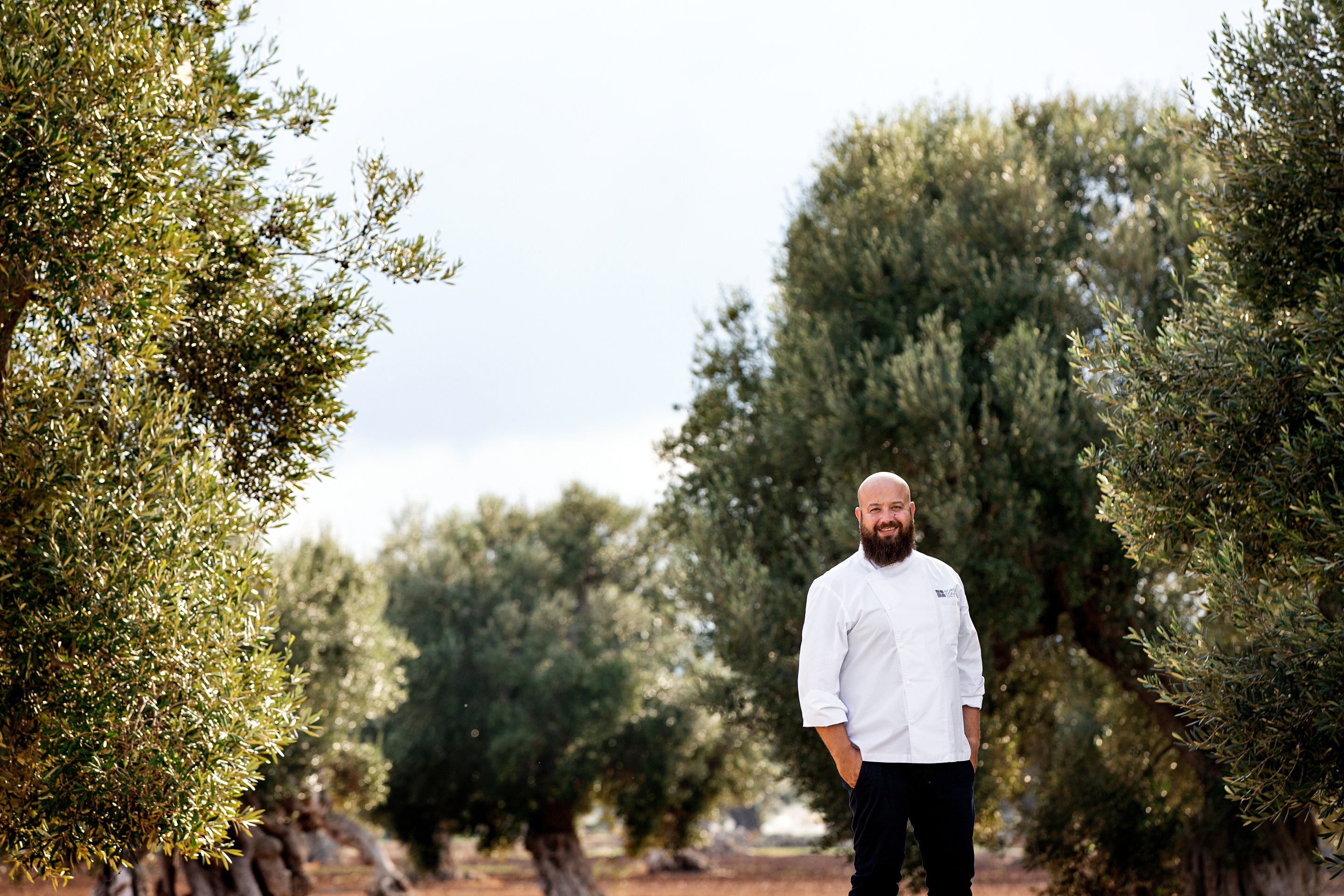 Chef Domingo Schingaro standing among olive trees in Puglia