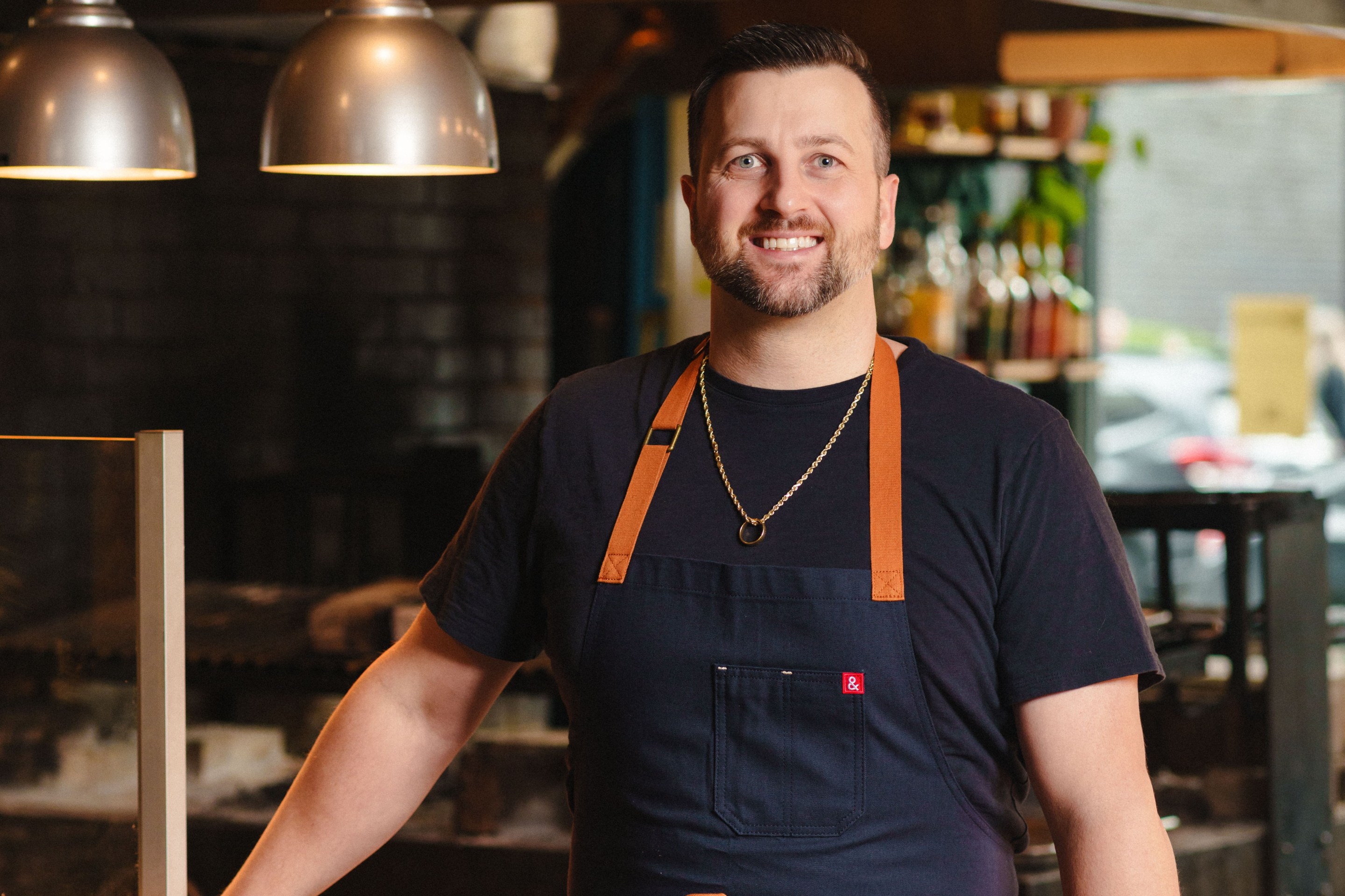 Portrait of Chef Gabriel Pascuzzi wearing a navy apron inside his Portland restaurant kitchen.