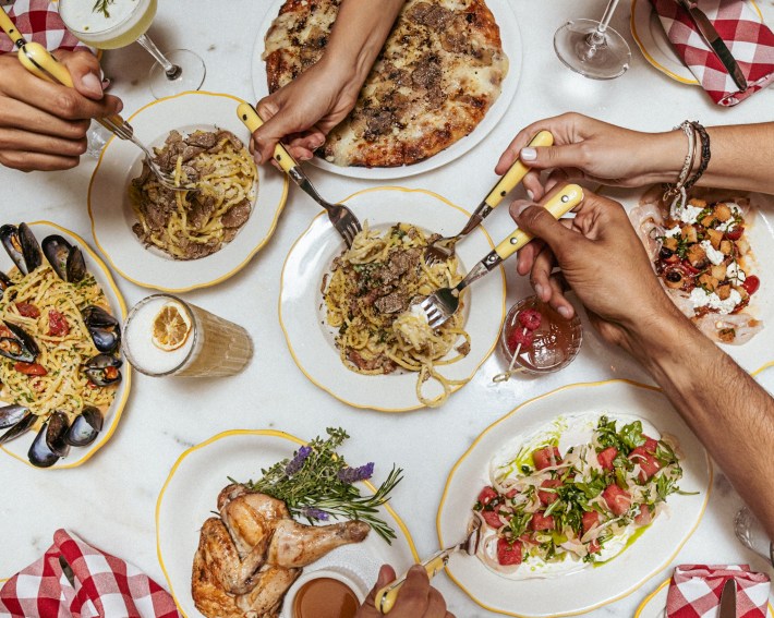 Guests gathered around a table sharing food and raising glasses during a family style Italian meal.