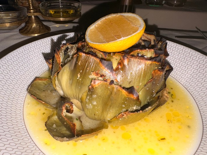 A classic stuffed artichoke arrives glistening with butter and topped with lemon.