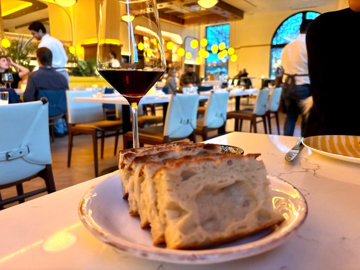 Glass of red wine and sliced focaccia on a marble table inside Costa Charleston.