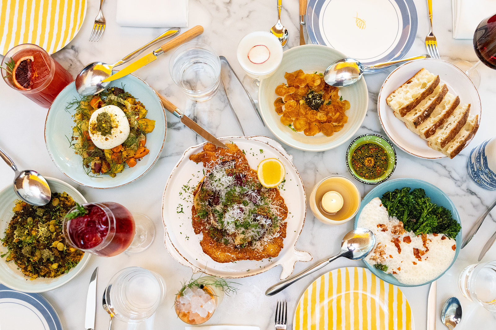 Overhead view of multiple Italian dishes including gnudi with caviar, seafood, greens, cocktails, and focaccia at Costa Charleston.