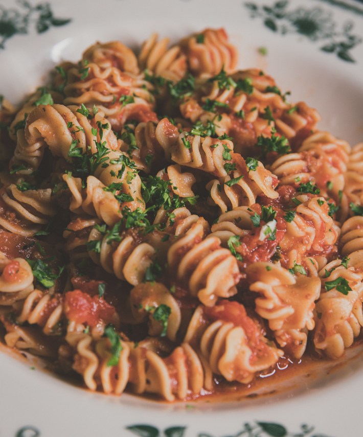 Pasta with red sauce and herbs in a white dish.