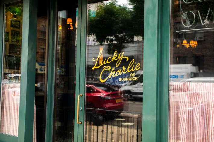 The front entrance of Lucky Charlie in Bushwick with the restaurant’s neon sign on the glass door.