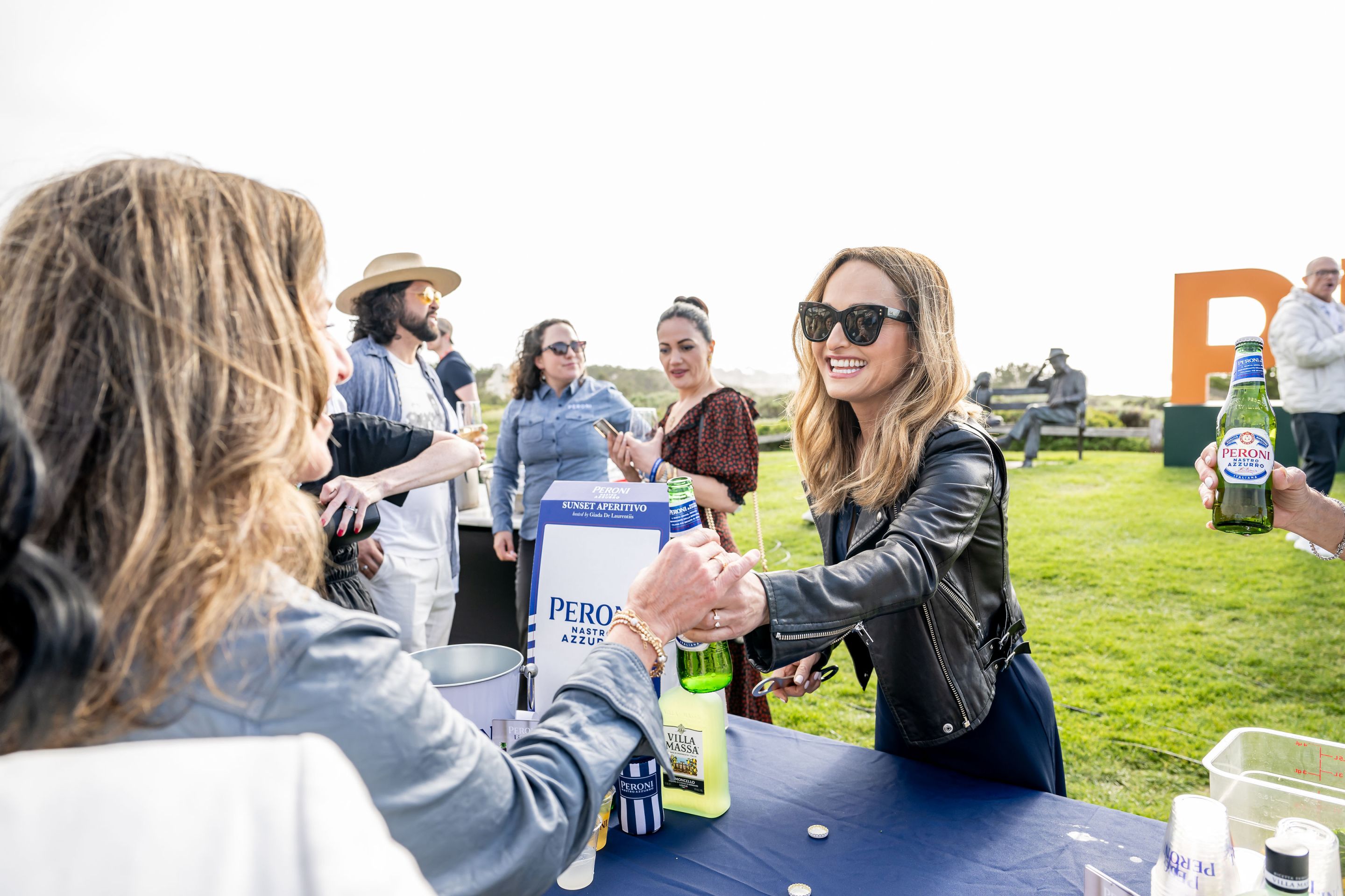 Giada De Laurentiis serving a Peroni beer to a guest at an outdoor festival event.