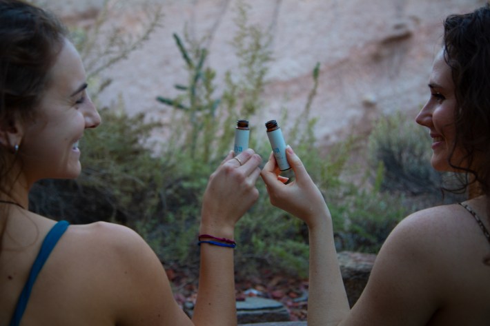 Two hands holding small bottles of Alya Health olive oil outdoors