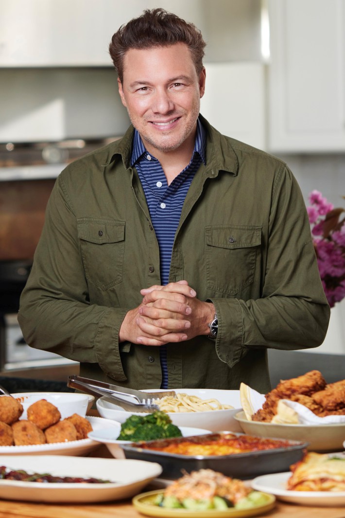 Chef Rocco DiSpirito standing at a restaurant table with wine glasses.
