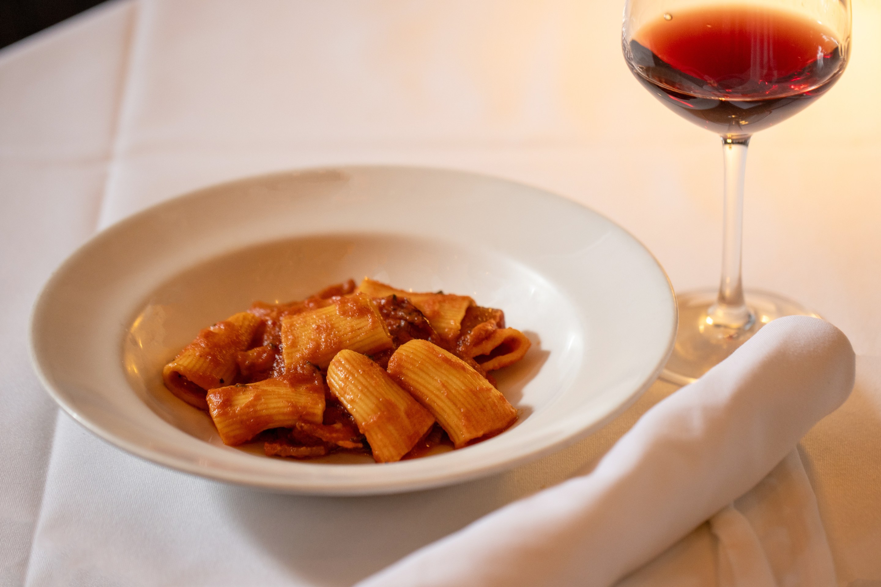Rigatoni Amatriciana paired with Roero DOCG red wine at dinner, part of Sip and Savor: Pairing European Wines and Deli Meats Campaign Co-funded by the European Union.