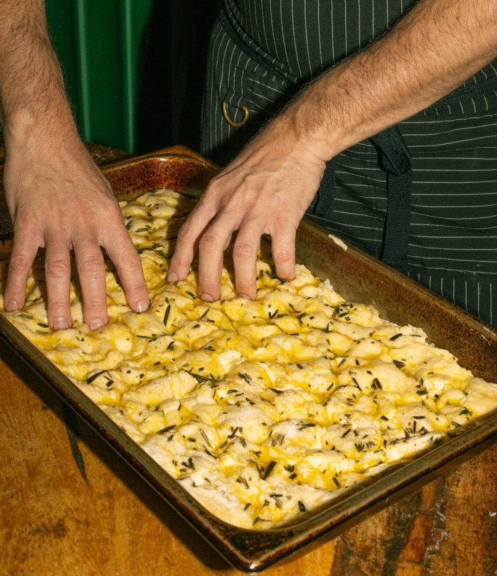 Hands pressing focaccia style dough with olive oil and herbs