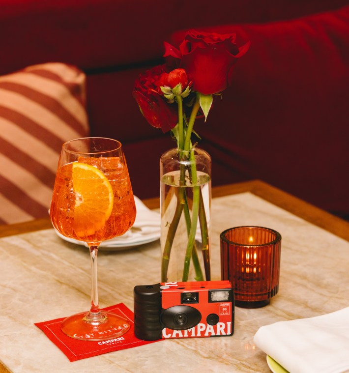 Campari Spritz cocktail with orange slice on table with red roses