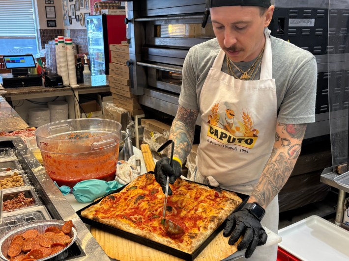 Square Roman-style pizza being topped with sauce in a pan