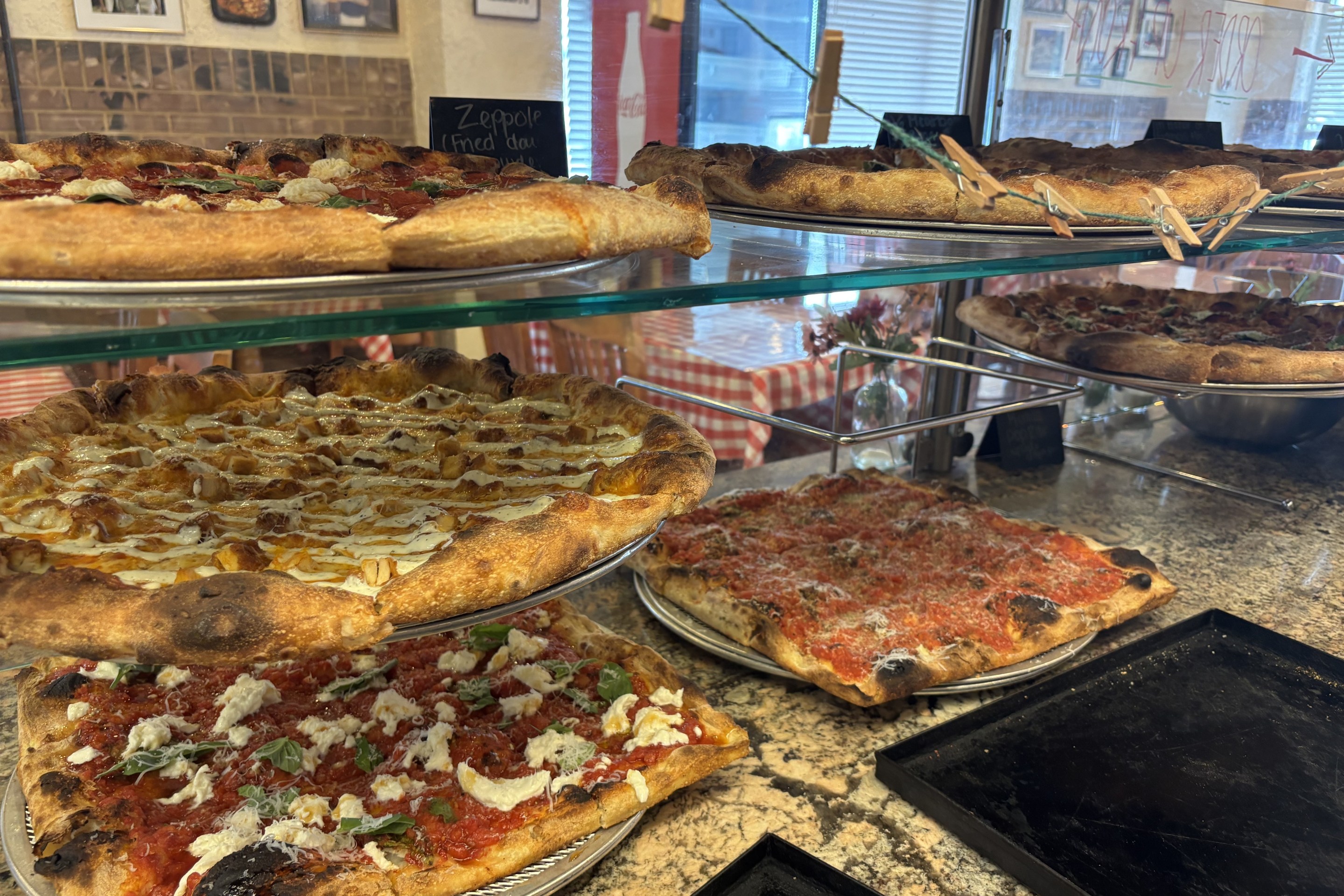 Assorted pizzas displayed in a glass case at Anto's PIzza Romana
