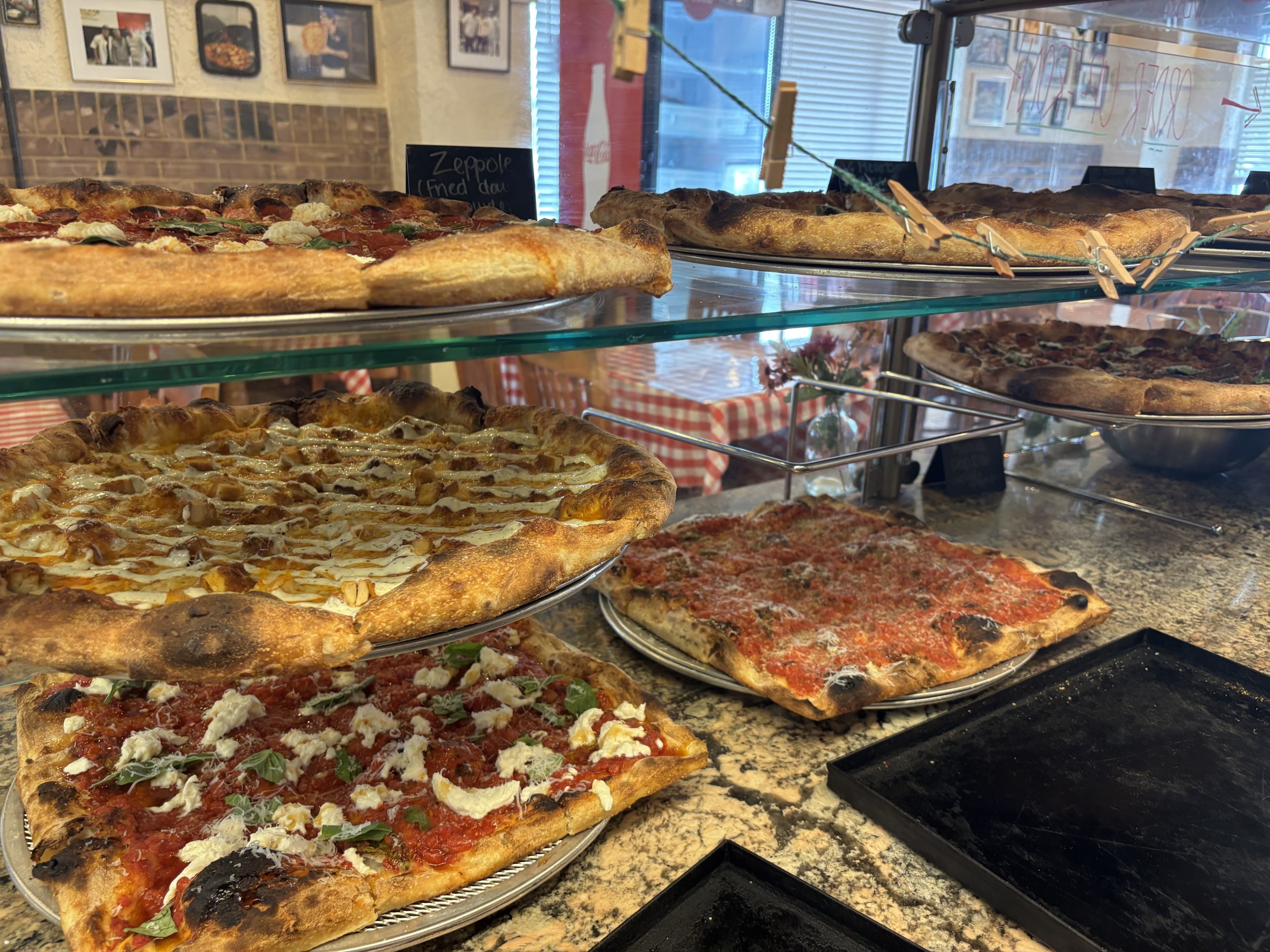 Assorted pizzas displayed in a glass case at Anto's PIzza Romana