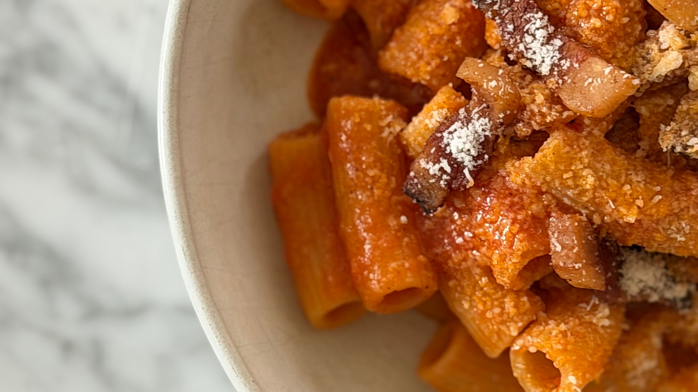Rigatoni amatriciana with crispy guanciale and pecorino romano in a white bowl.