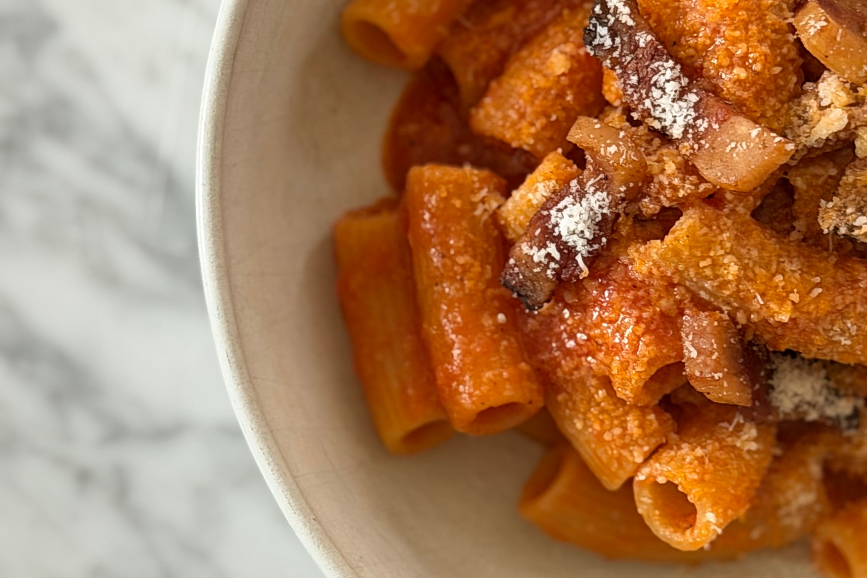 Rigatoni amatriciana with crispy guanciale and pecorino romano in a white bowl.