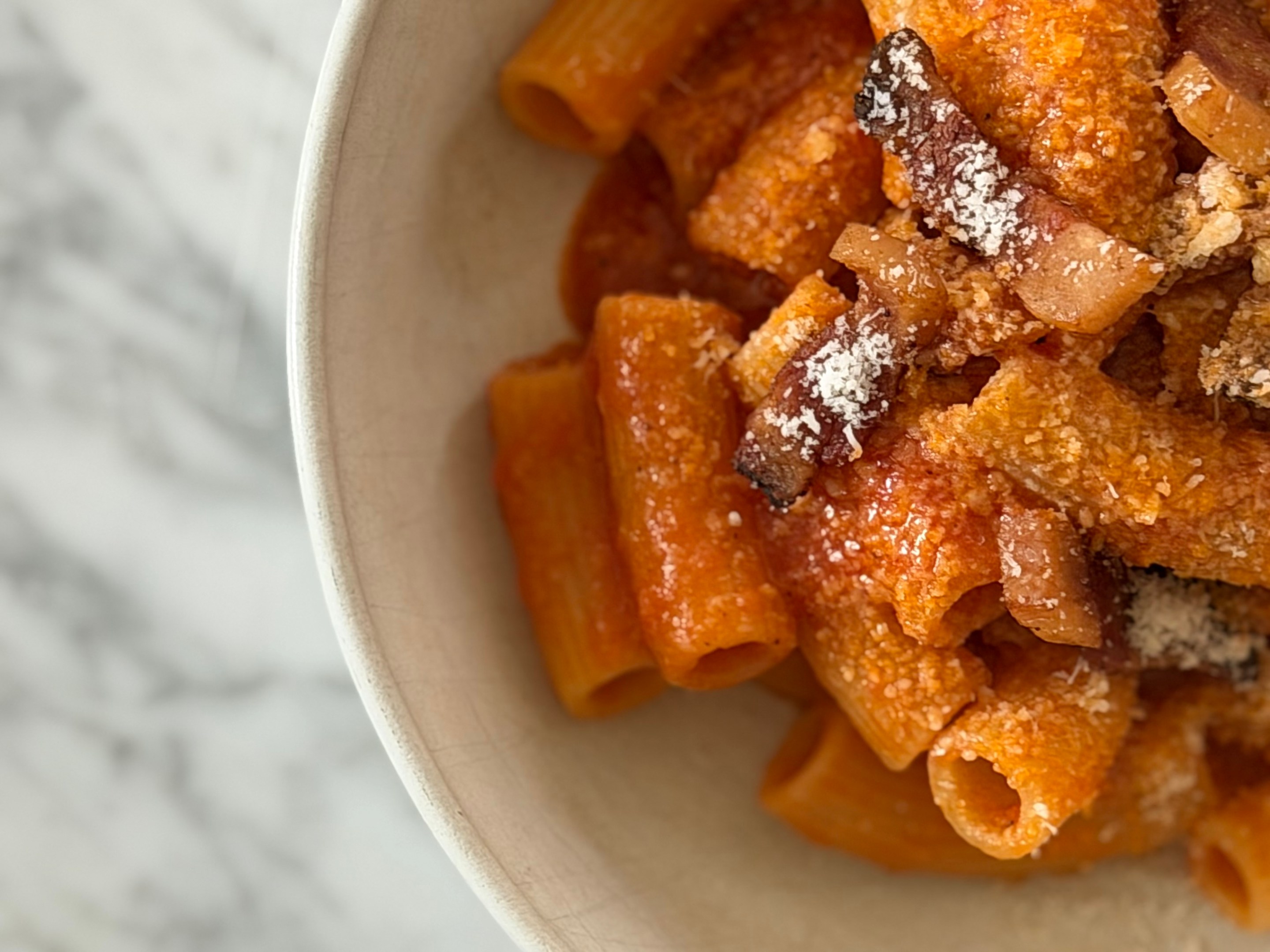 Rigatoni amatriciana with crispy guanciale and pecorino romano in a white bowl.