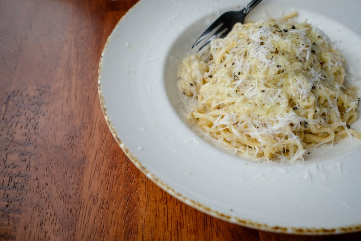 Plate of cacio e pepe pasta topped with grated cheese and black pepper.