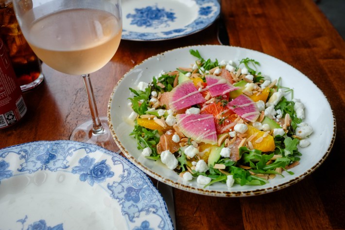Citrus avocado salad with grapefruit, orange, goat cheese, and almonds on a plate with a glass of white wine.