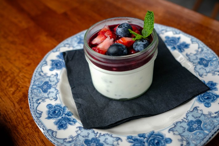 Glass jar of panna cotta topped with berry compote, strawberries, blueberries, and mint.