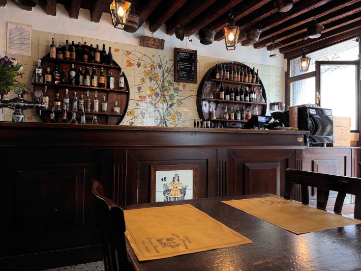 Interior of Osteria alla Caneva with wooden tables, wine bottles, and rustic decor
