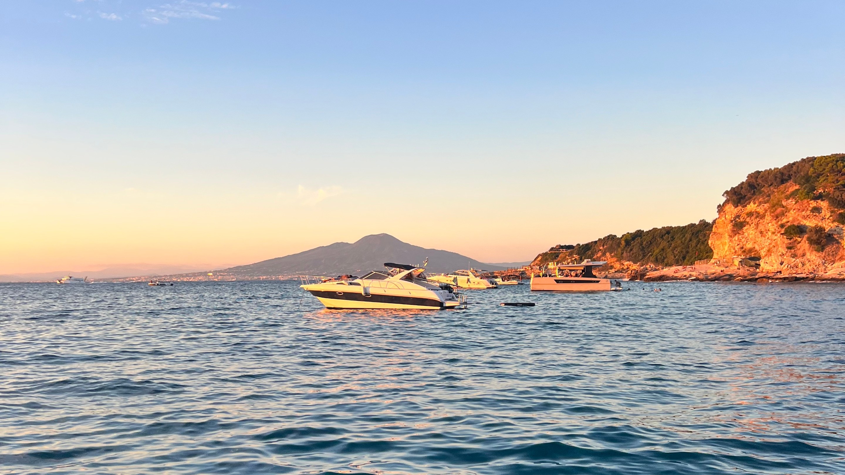 Boats floating off the Sorrento coastline at sunset with Mount Vesuvius in the distance.