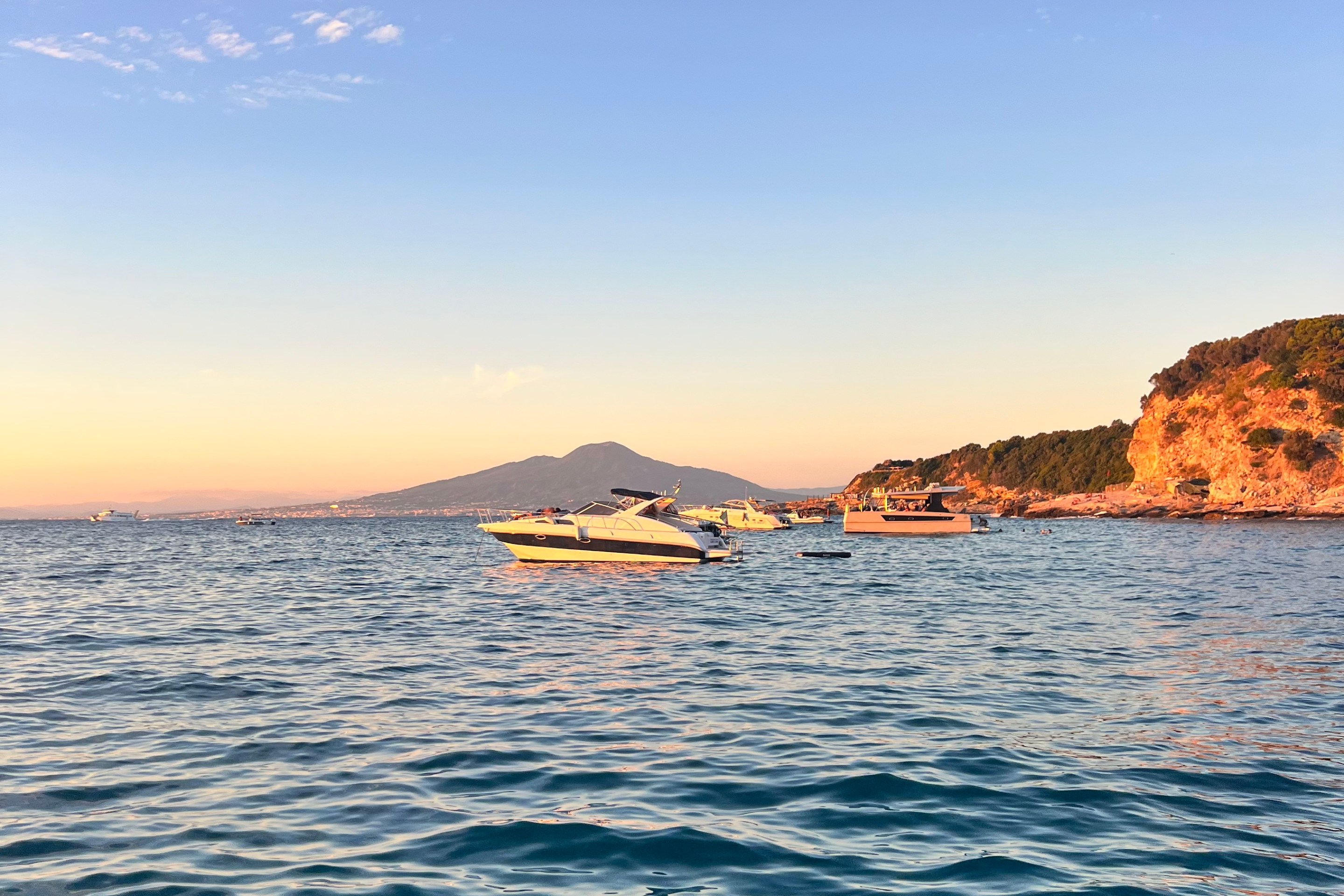 Boats floating off the Sorrento coastline at sunset with Mount Vesuvius in the distance.