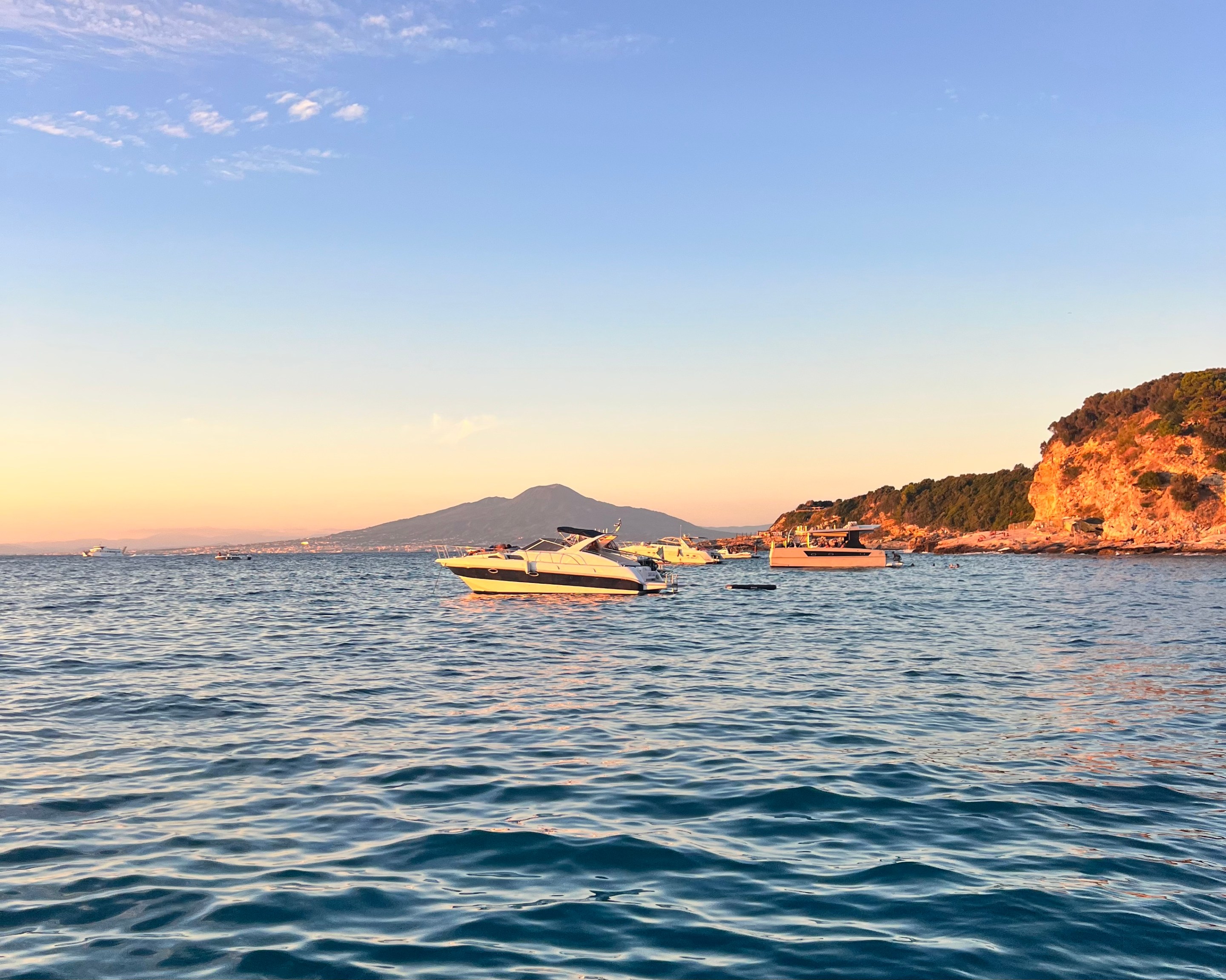 Boats floating off the Sorrento coastline at sunset with Mount Vesuvius in the distance.