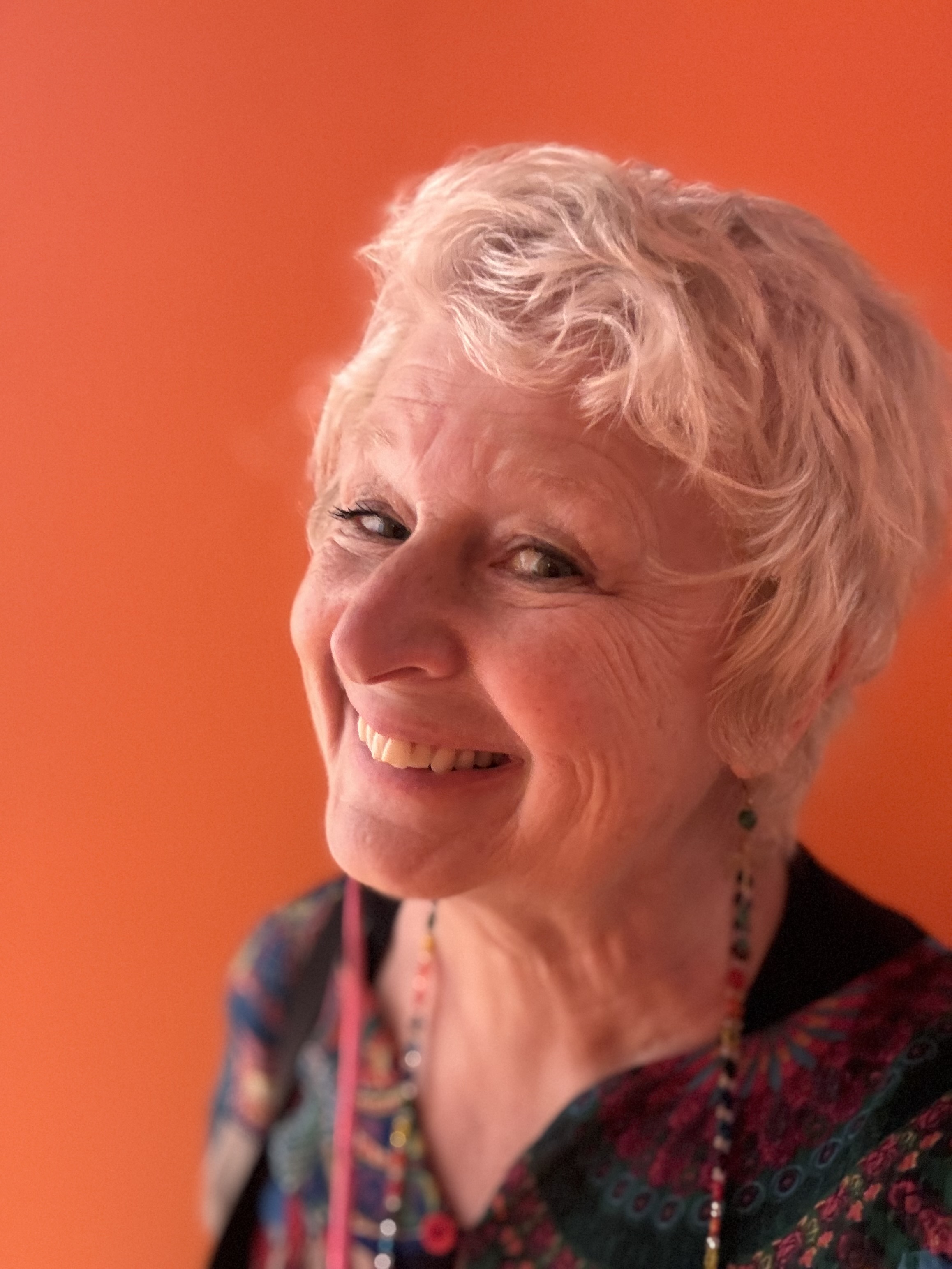 Headshot of Sharla Ault, pictured with an orange background, smiling.