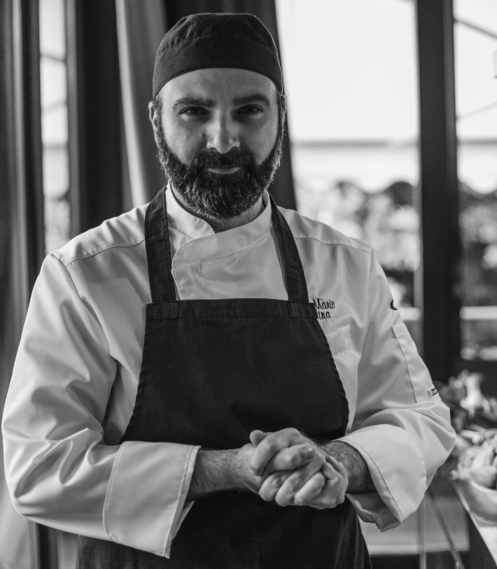 Portrait of Sicilian chef Mario Traina wearing a chef coat and apron in a restaurant setting.
