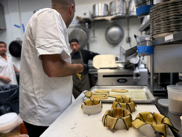 Chef preparing eggplant-lined ramekins for Sicilian timballo in a restaurant kitchen