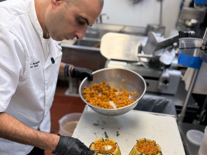 Chef filling eggplant-lined ramekins with anelletti pasta and ragù