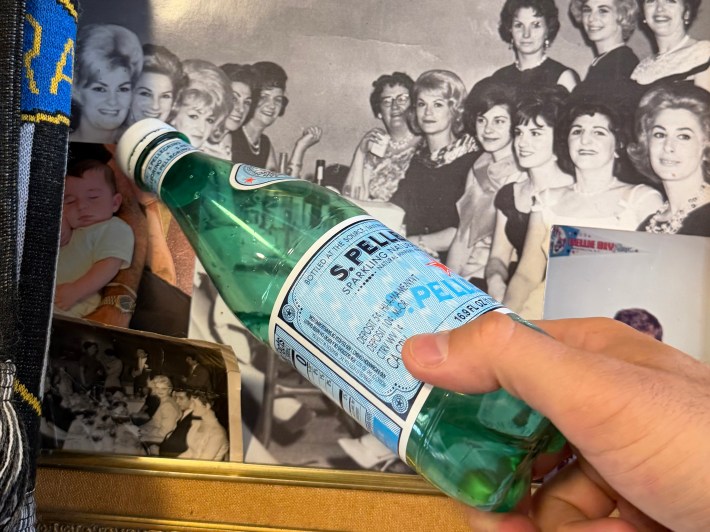 San Pellegrino bottle held in front of vintage family photos inside Regina’s Grocery.