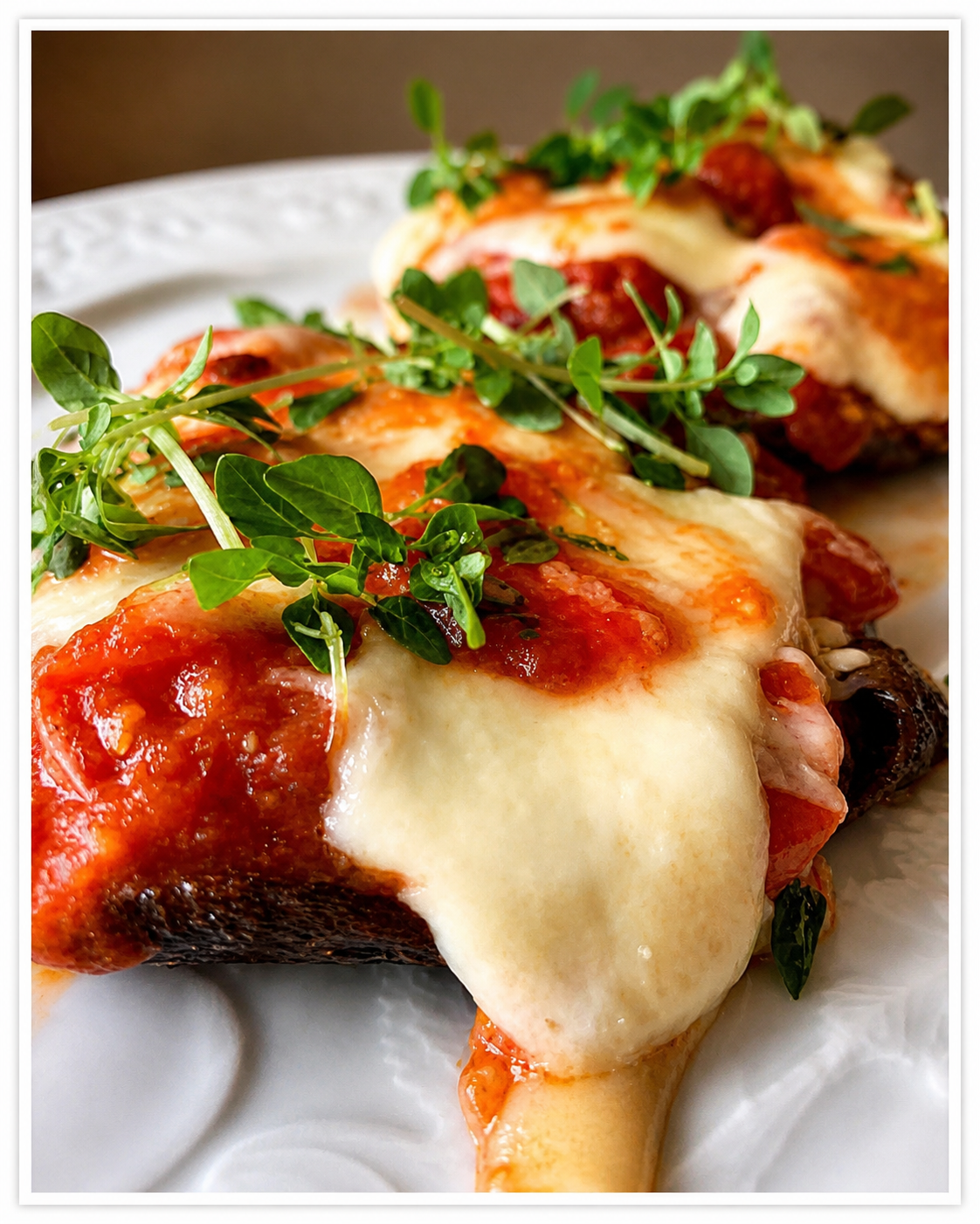 Close up of grilled portobello mushroom parmigiana with melted mozzarella cheese and tomato sauce on a white plate