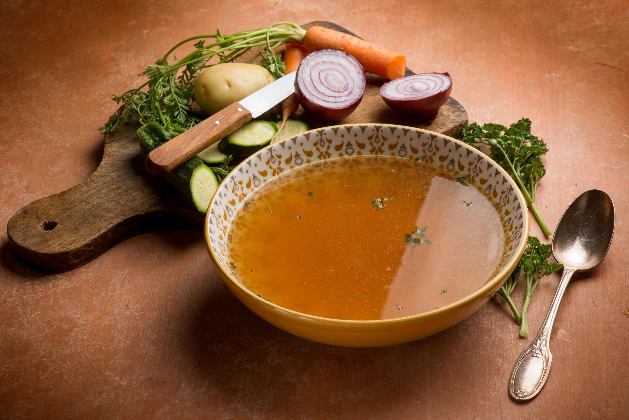 A rustic Italian kitchen with broth simmering beside vegetable scraps and Parmesan rinds