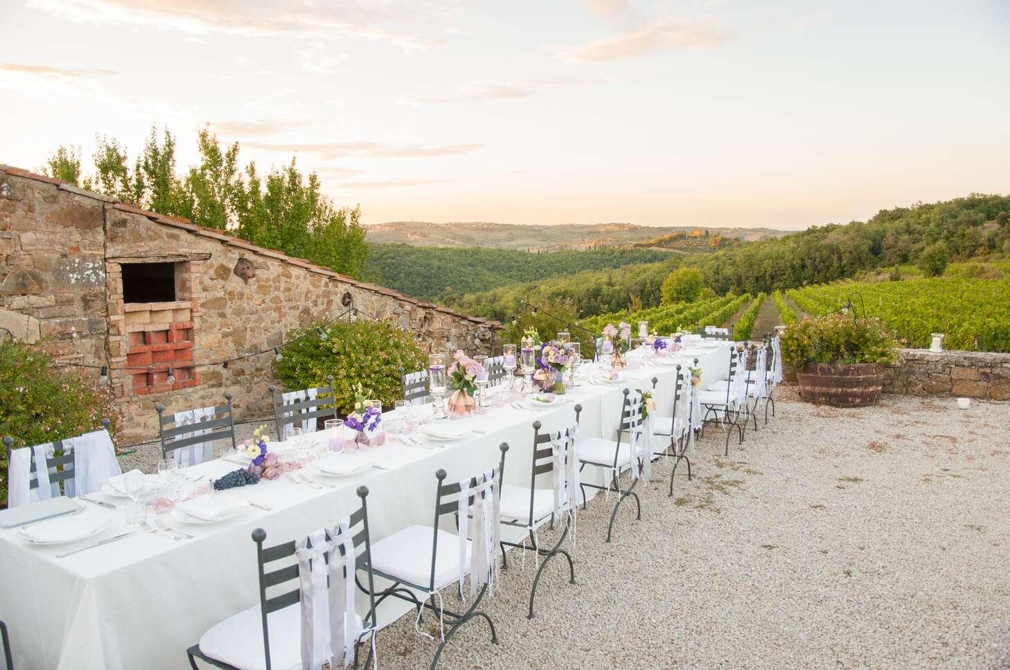 An outdoor Italian wedding feast stretches across a long table with grape vineyards in the background.