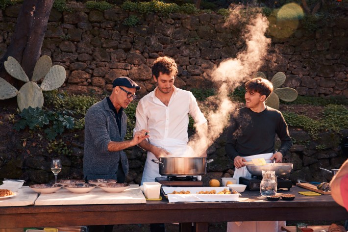 Stanley Tucci cooking with Sicilian chefs outdoors.