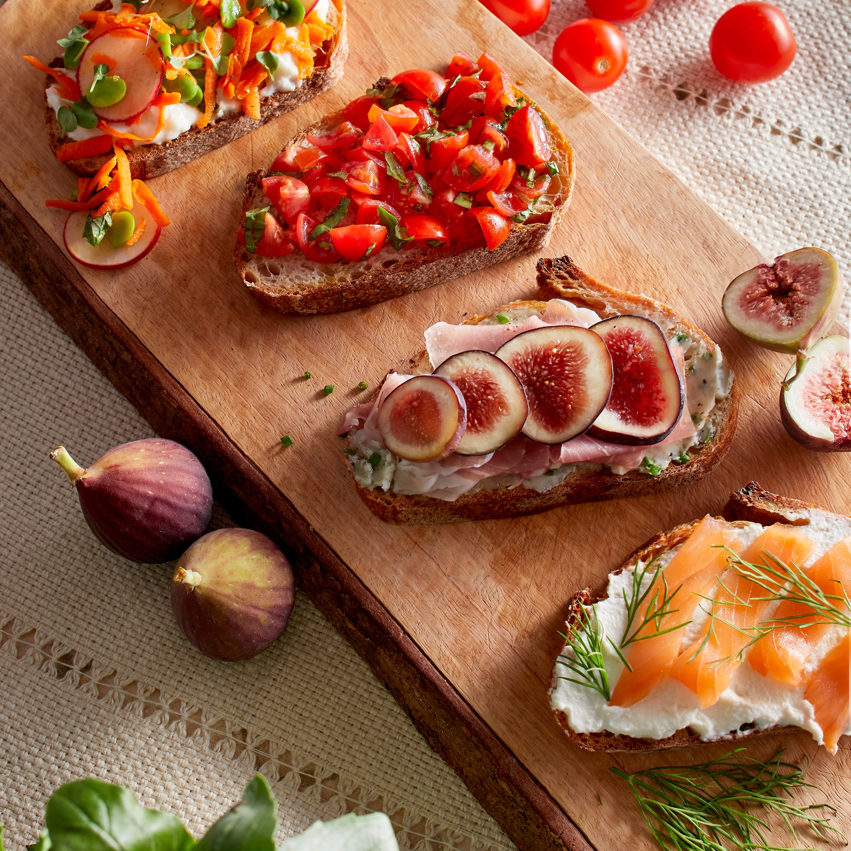 A rustic bruschetta board topped with fresh tomatoes, basil, burrata, prosciutto, olives, roasted vegetables, and toasted bread