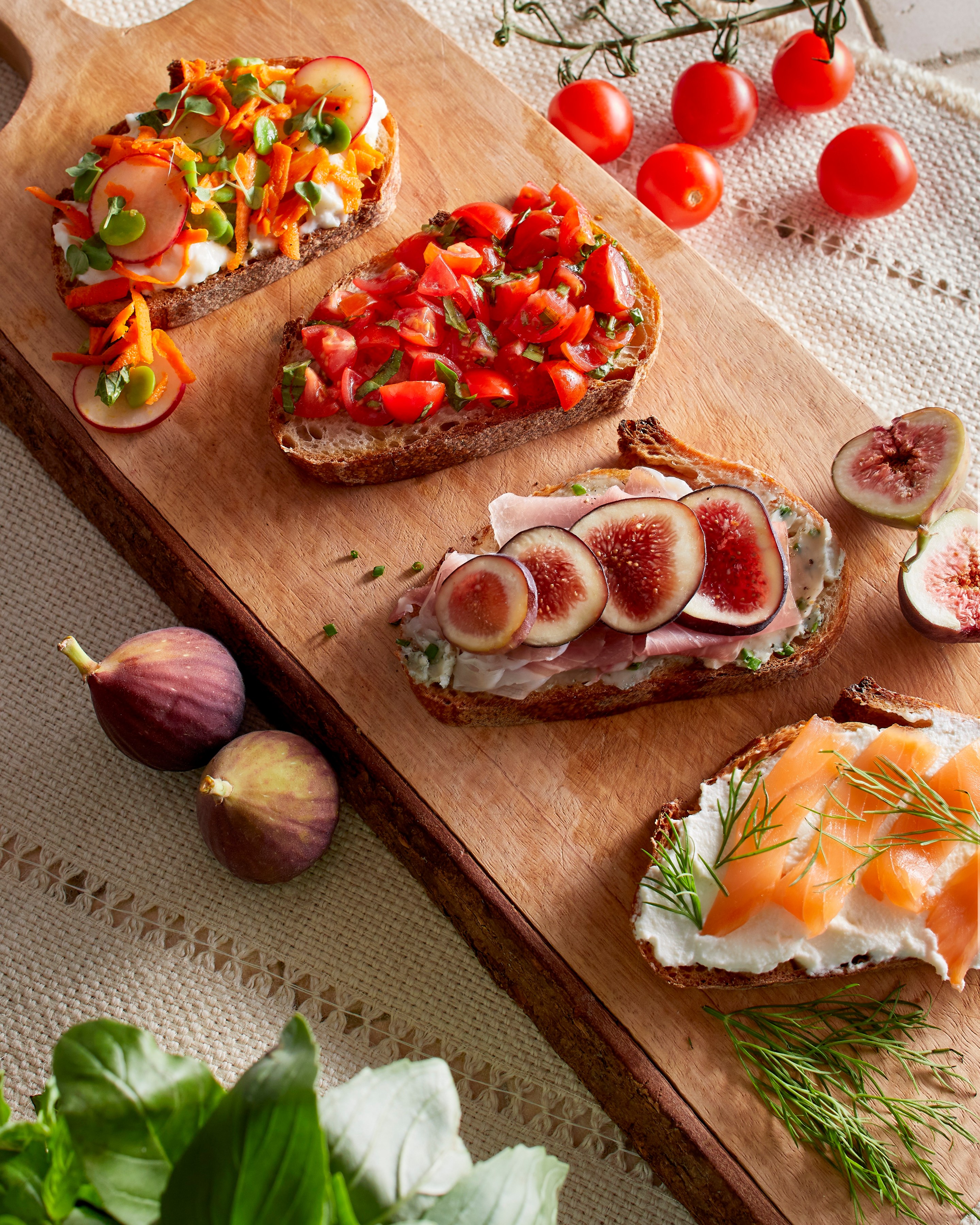 A rustic bruschetta board topped with fresh tomatoes, basil, burrata, prosciutto, olives, roasted vegetables, and toasted bread