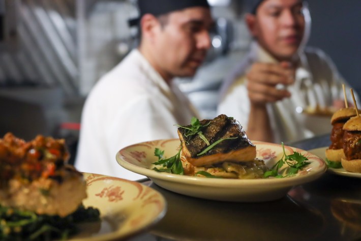 A plated entrée at The Little Owl with chefs working in the background.